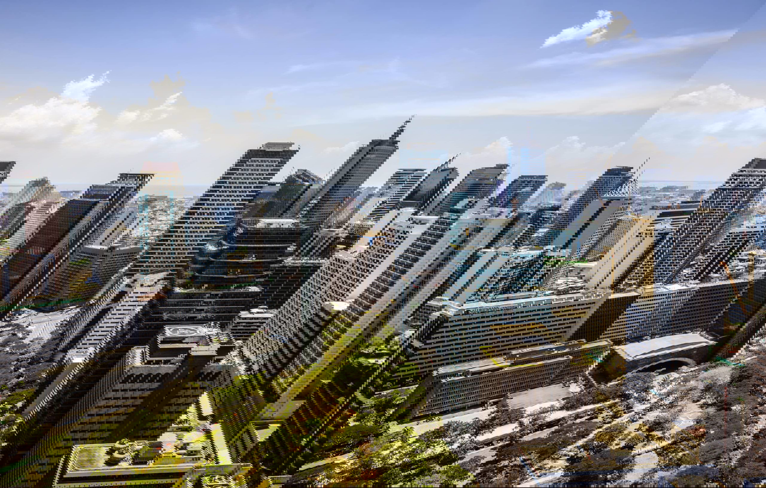 Aerial view of a modern city skyline with numerous skyscrapers and high-rise buildings. The foreground features a green park with trees. The Philippines, known for being a top destination where major corporations outsource their business needs, boasts clear skies dotted with clouds.