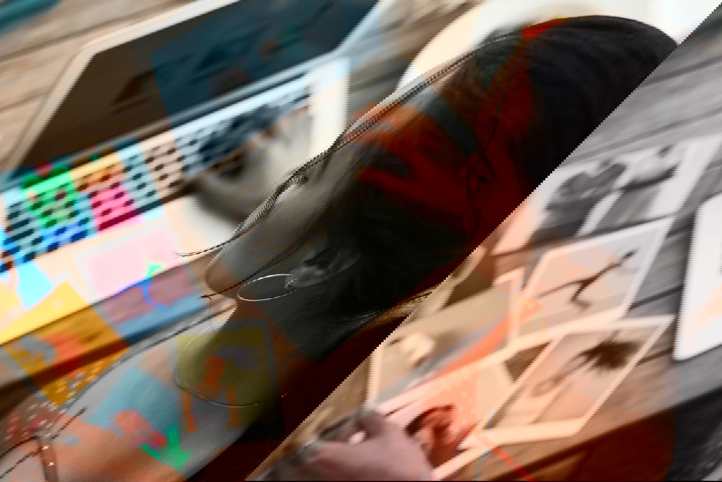 A woman in a red polka dot dress works on a laptop at a wooden table, exploring Fancy Hands alternatives. Colorful photos are spread out beside her. She has dark hair tied back and is wearing hoop earrings.