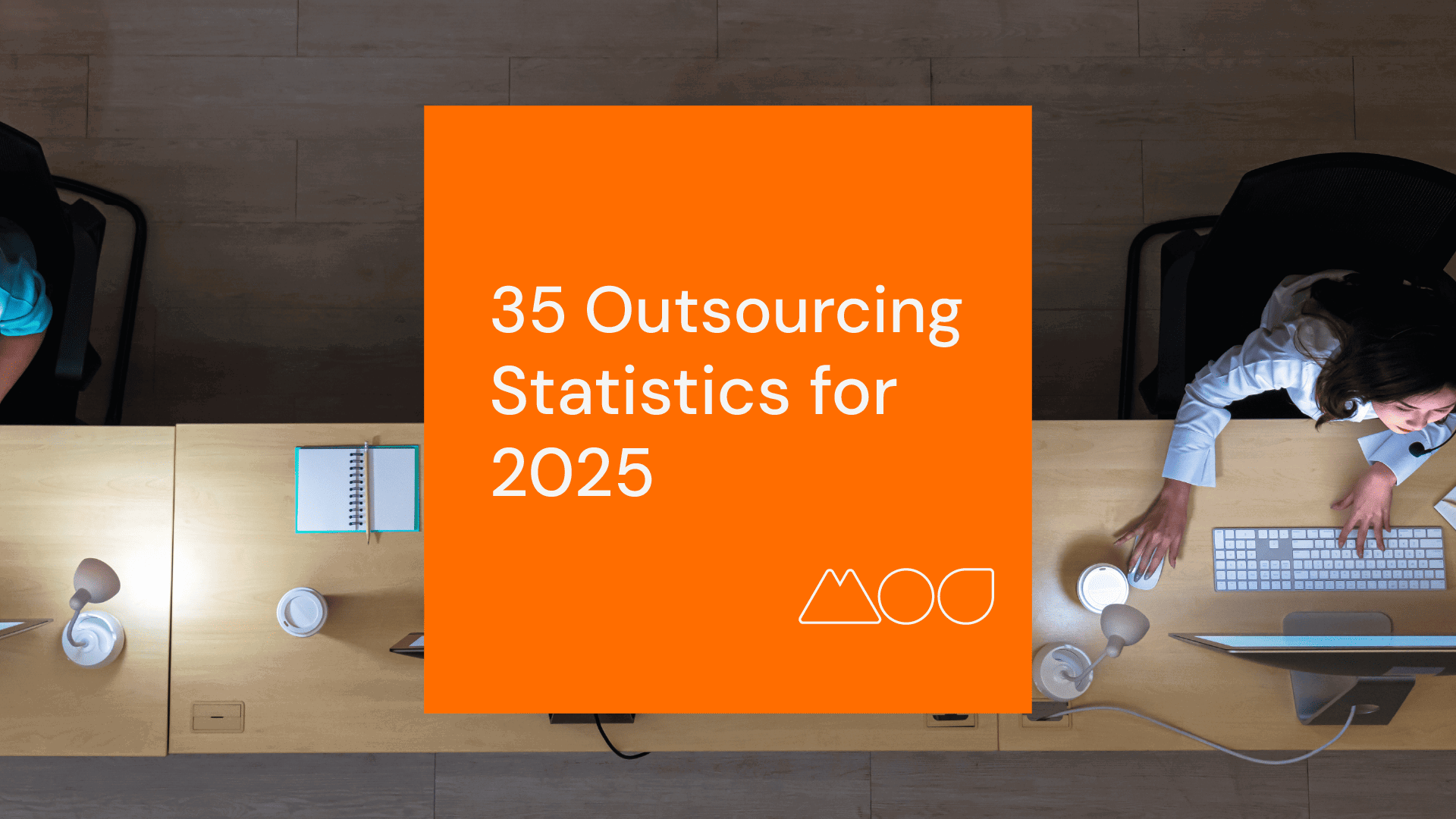 Top view of two people sitting at a table with computers, lamps, and notebooks. An orange square in the middle reads 35 of the Most Powerful Outsourcing Statistics for 2024 by MyOutDesk, with a small logo underneath.