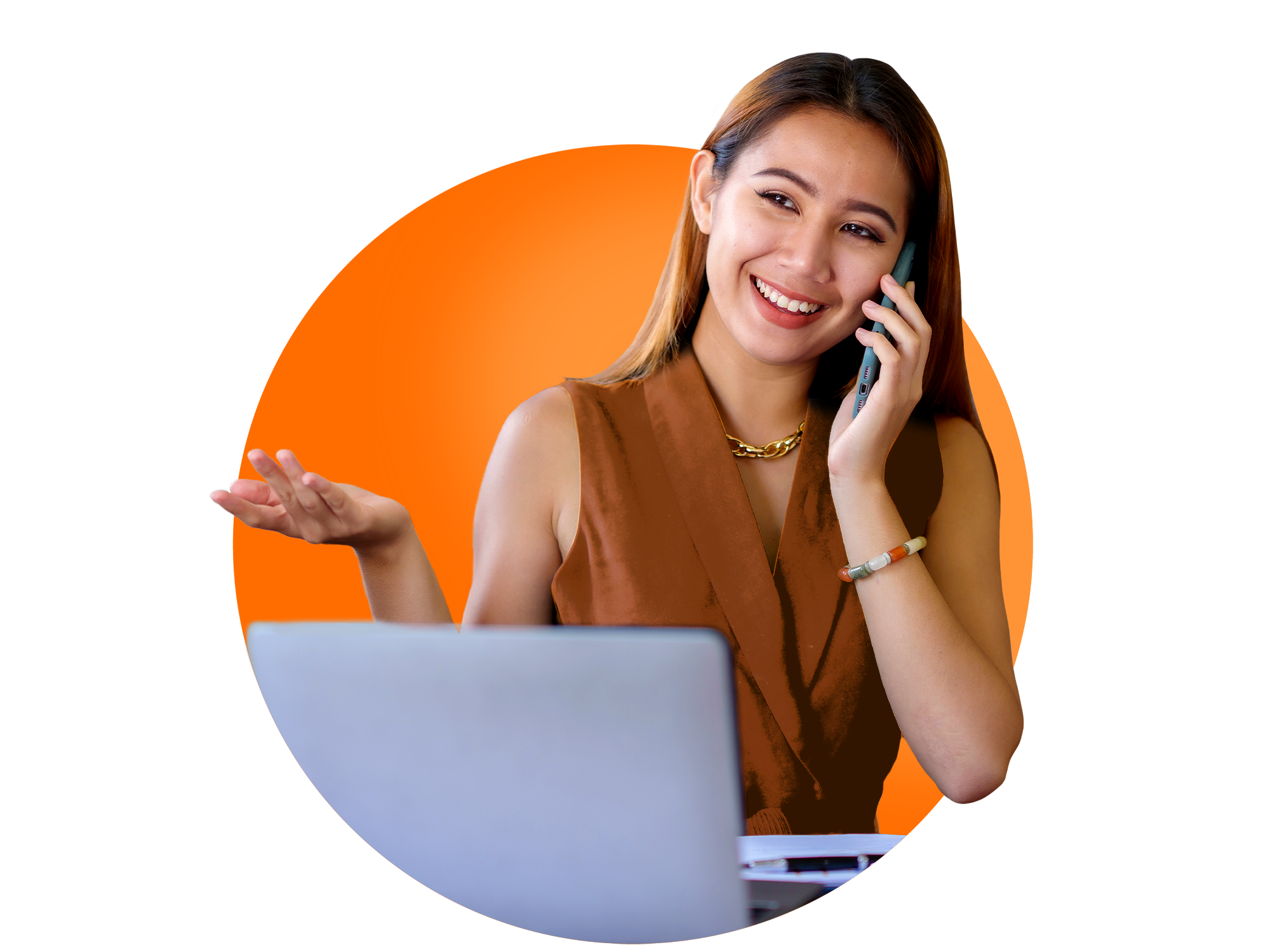A young woman on the phone, in front of a laptop, smiling and gesturing.